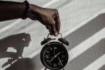 Close-up of a hand holding a vintage alarm clock casting shadows in daylight.