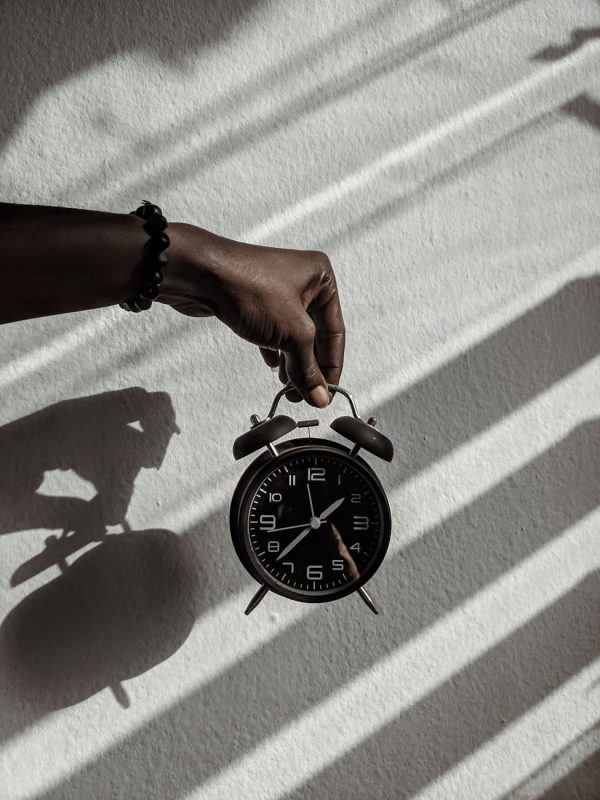 Close-up of a hand holding a vintage alarm clock casting shadows in daylight.