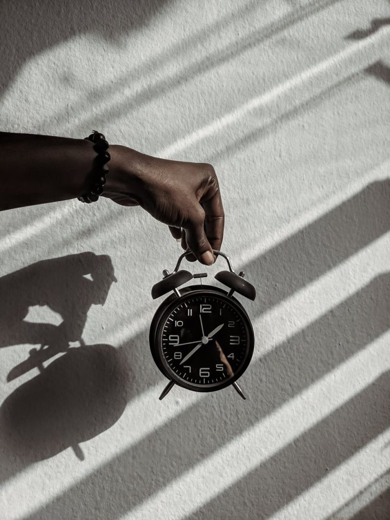 Close-up of a hand holding a vintage alarm clock casting shadows in daylight.