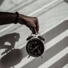 Close-up of a hand holding a vintage alarm clock casting shadows in daylight.