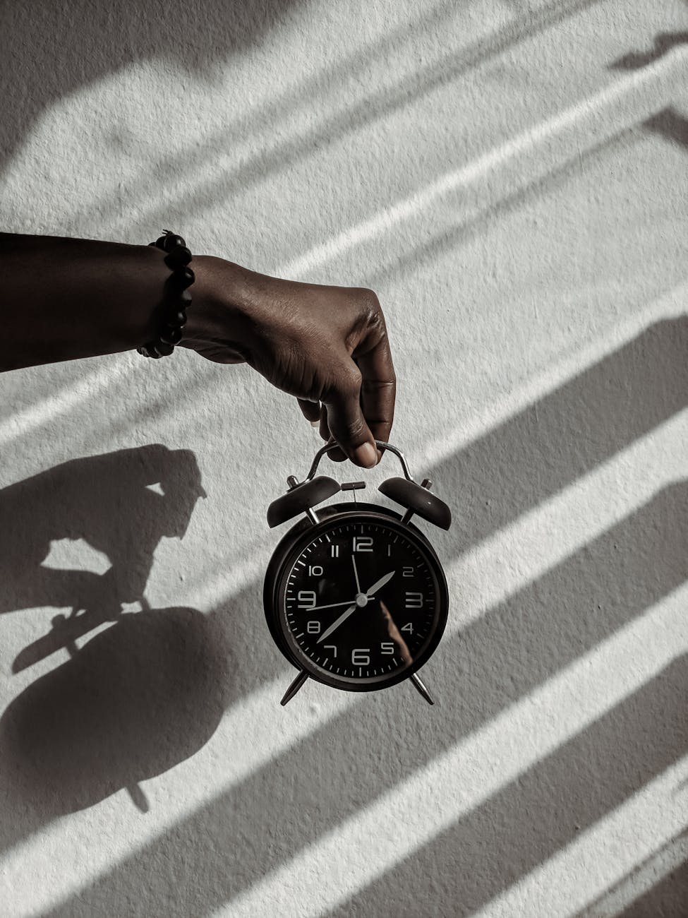 Close-up of a hand holding a vintage alarm clock casting shadows in daylight.