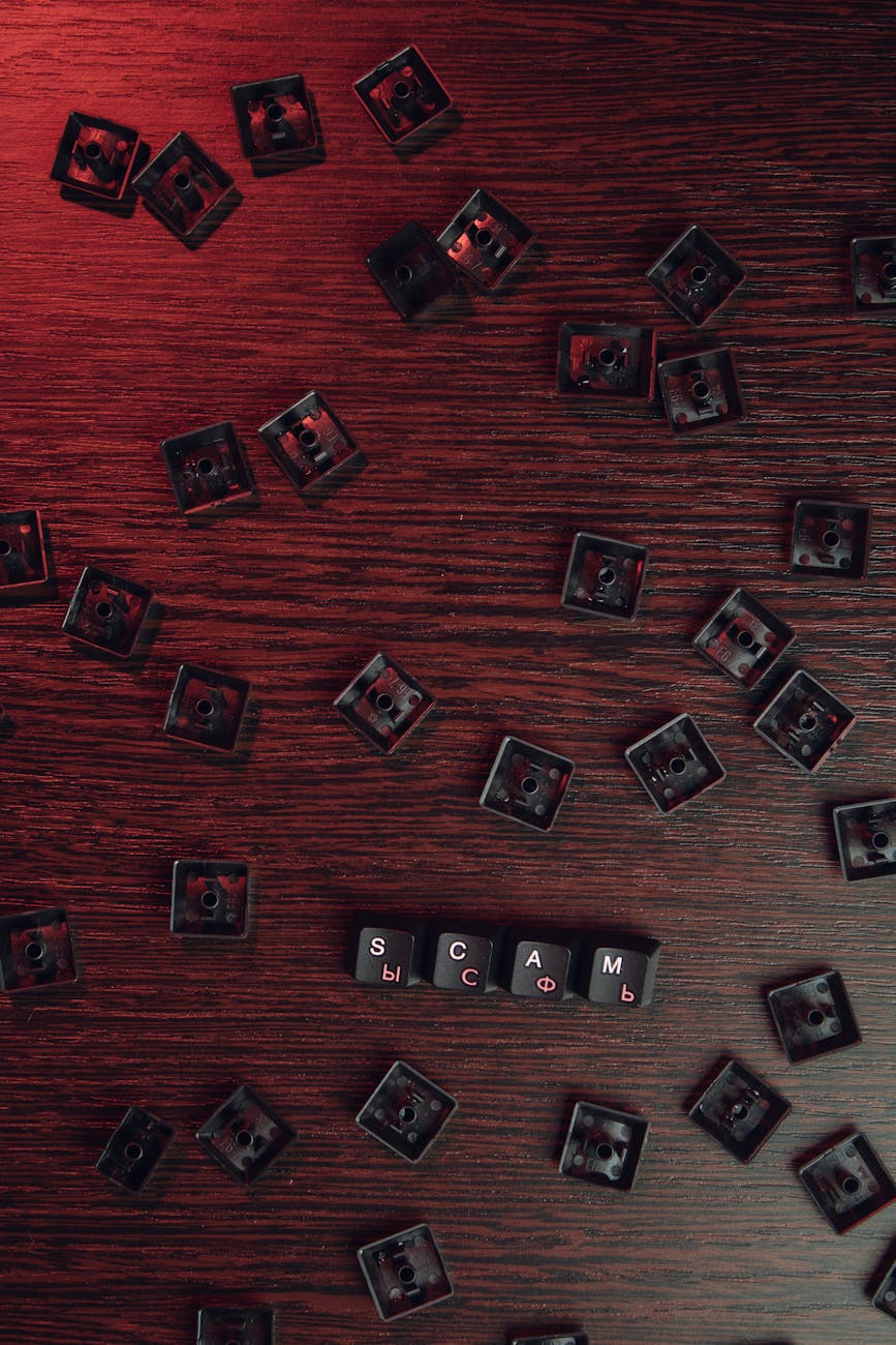 Scattered keyboard keys spelling 'SCAM' on a red-lit wooden surface, symbolizing online fraud.