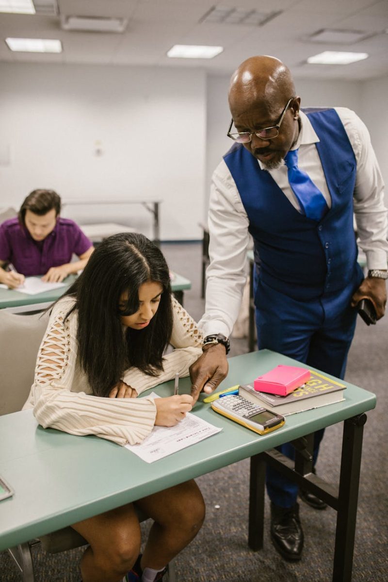 Educator assisting student during an exam in a classroom setting, emphasizing support in education.