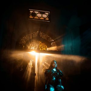 A woman in dramatic lighting poses in an atmospheric setting with rays of light.