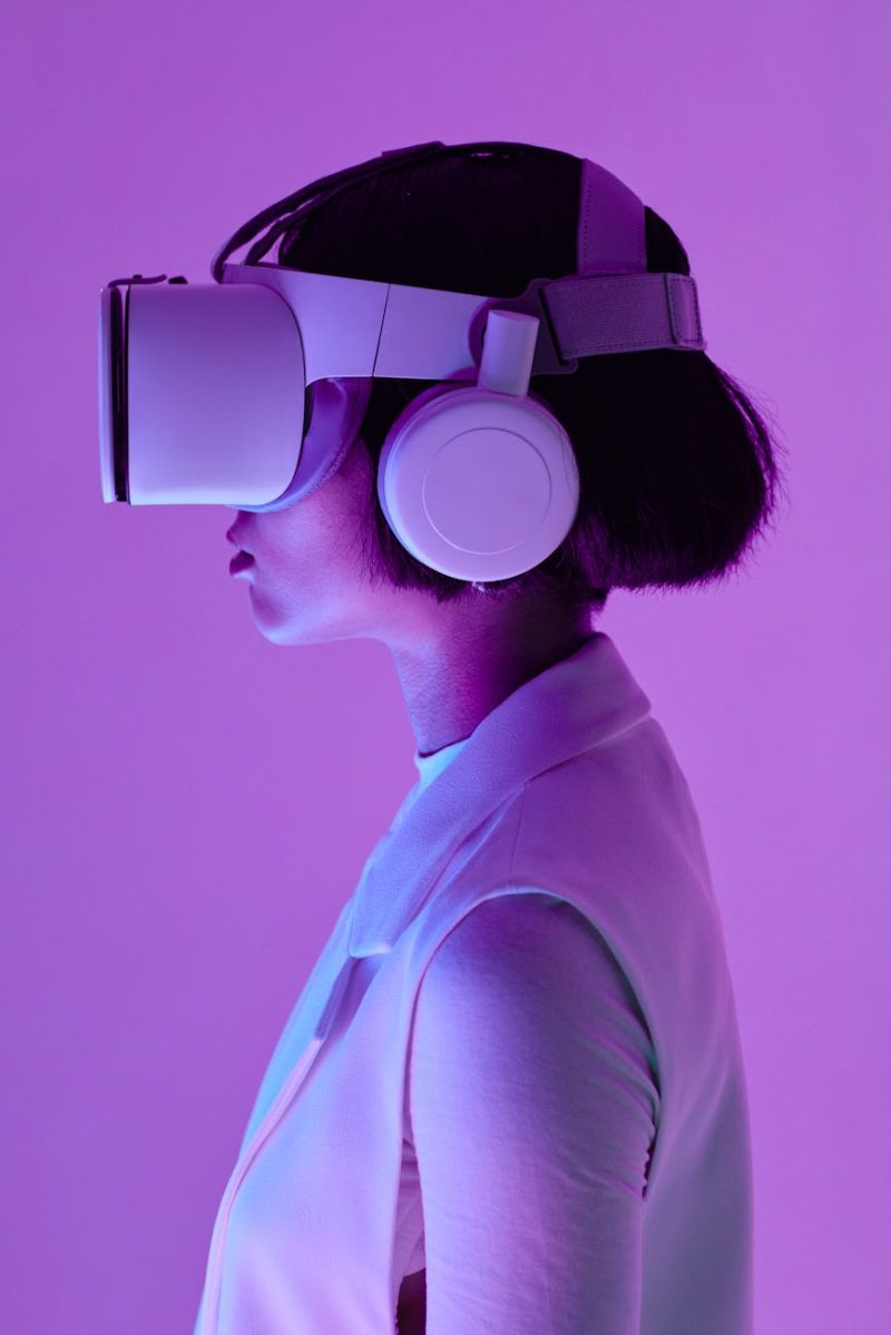 Side profile of a woman wearing VR goggles in a studio with purple lighting, embodying future tech.