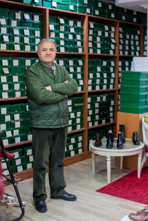 Full body of calm ethnic male customer in uniform standing with crossed arms in shoe store against shelves with boxes and looking at camera