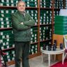 Full body of calm ethnic male customer in uniform standing with crossed arms in shoe store against shelves with boxes and looking at camera
