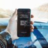 Close-up of a hand holding a smartphone in a car, highlighting technology and motivation.