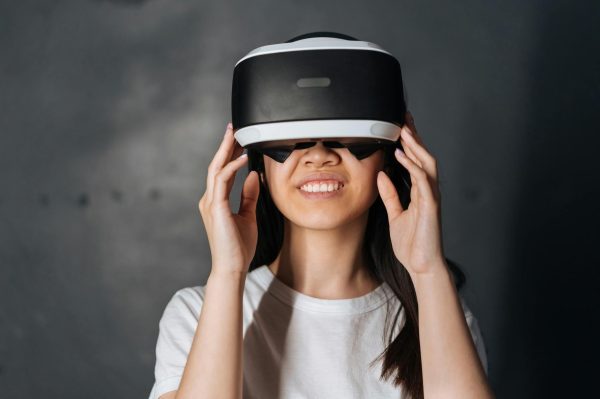 Smiling young woman immersed in virtual reality, wearing VR headset indoors.