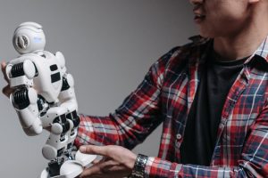 An adult man examines a humanoid robot against a gray background, exploring modern technology.