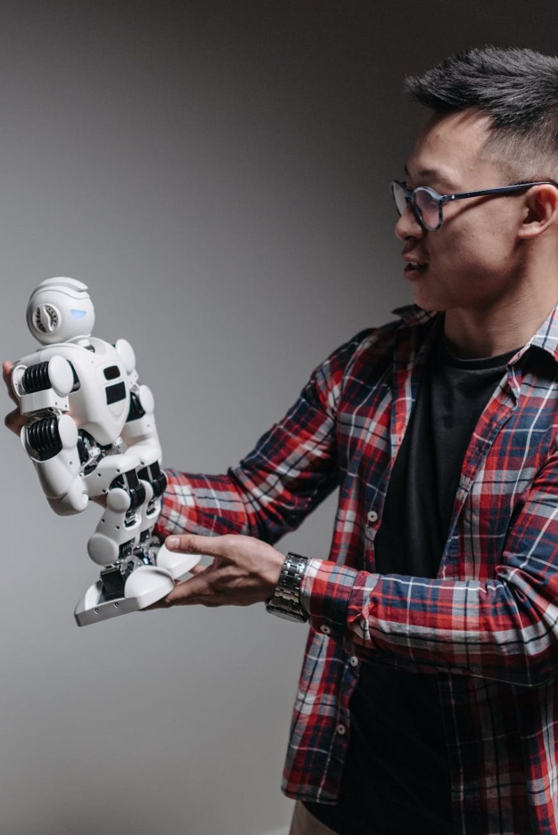 An adult man examines a humanoid robot against a gray background, exploring modern technology.
