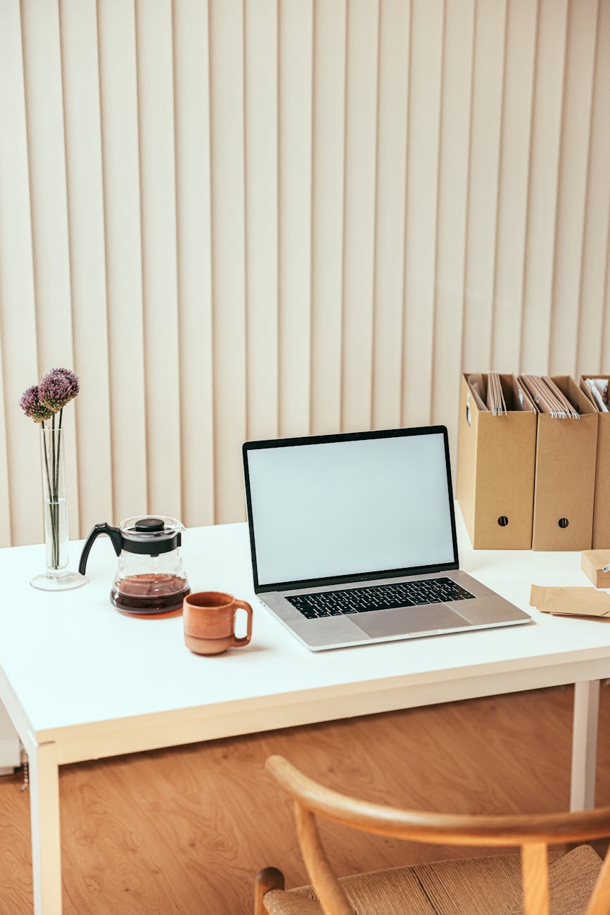 A clean and minimalistic office setup with a laptop, coffee carafe, and stylish decor.